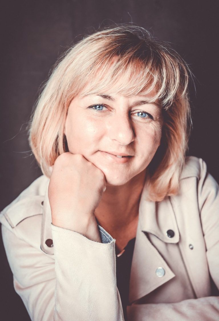 Porträtaufnahme von Doreen Unglaube mit aufgestütztem Kinn Porträt einer blonden Frau mit blauen Augen in heller Bikerjacke, die lächelnd ihr Kinn auf die Hand stützt.